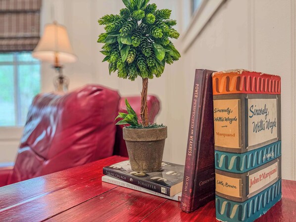 A small potted plant on a stack of books, a red couch, and a lamp in the background. - Hummingbird Home - a Craftsman Bungalow (Mobile)