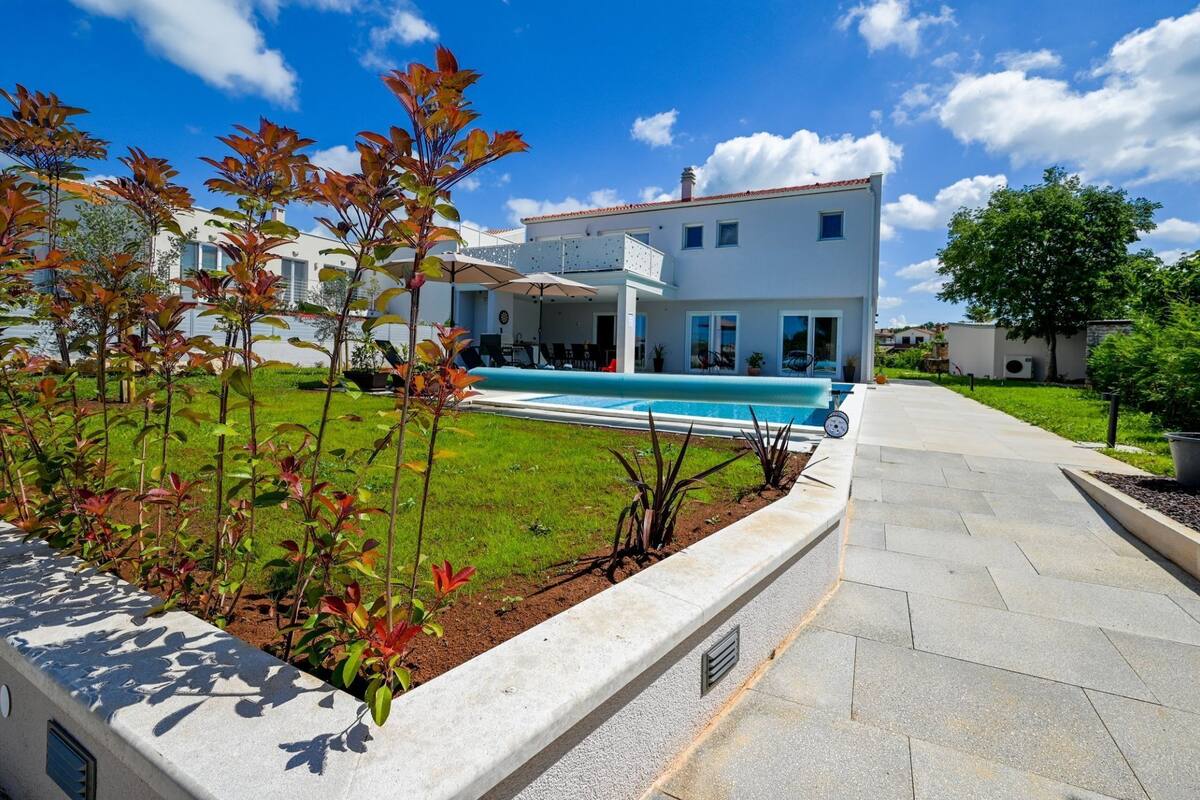 A modern two-story house with a swimming pool, a covered patio, and a well-maintained garden.