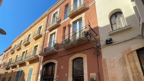 A multi-story building with balconies, a door with a sign, and a brick facade. - Lluria 11 (Tarragona)