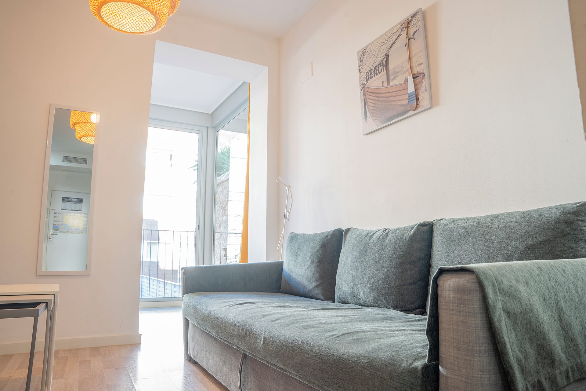 Een moderne woonkamer met een grijze bank, een klein tafeltje en een wanddecoratie met daarop een strandtafereel.