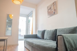 En moderne stue med en grå sofa, et lille bord og et billede på væggen, der viser et strandmotiv.