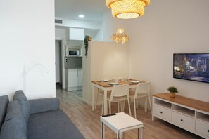 Un salon moderne avec un canapé gris, une table à manger dressée pour quatre personnes et un téléviseur fixé au mur.
