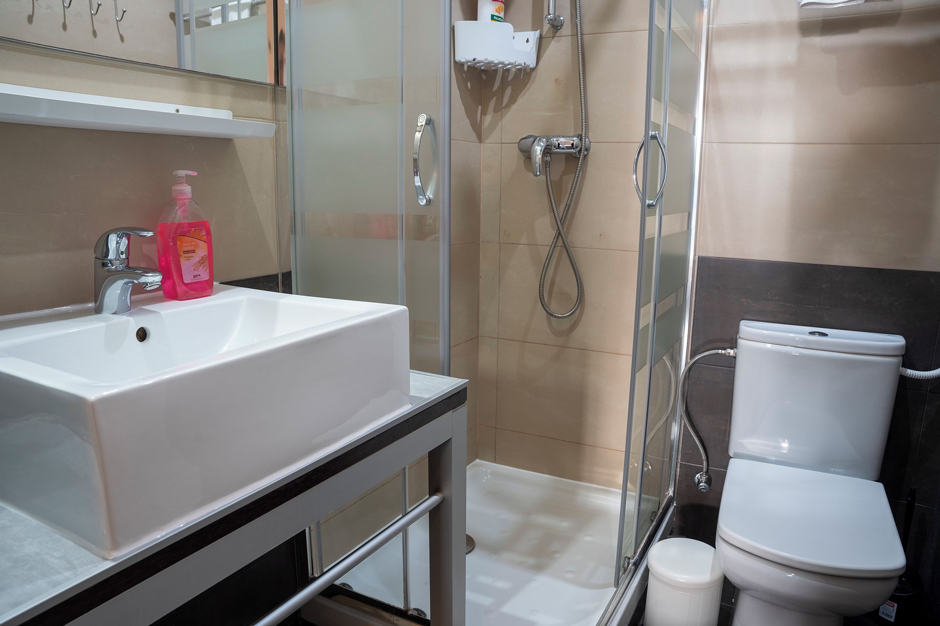 Een badkamer met een wit wastafelmeubel, een toilet en een douchecabine van glas.