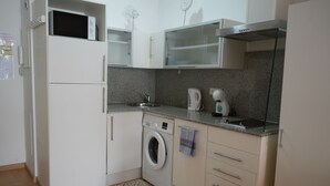 A compact kitchen with a washing machine, microwave, and a small sink. - Lluria 11 (Tarragona)