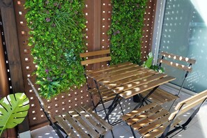 Un banc en bois doté d’une structure métallique, entouré d’un jardin vertical composé de feuillage verdoyant et de fleurs violettes, le tout adossé à un mur en treillis de couleur marron.