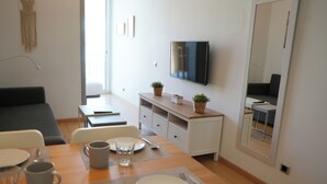 A modern, well-lit dining area with a wooden table set for two, a television mounted on the wall, and a small plant on the sideboard. - Lluria 11 (Tarragona)
