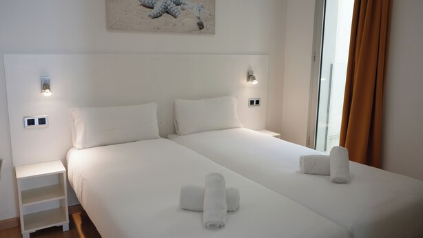 A hotel room with a large bed, two bedside tables, a wall-mounted light, and a painting above the bed. - Lluria 11 (Tarragona)