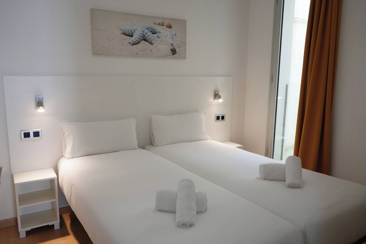A hotel room with a large bed, two bedside tables, a wall-mounted light, and a painting above the bed.