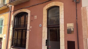 A building with a stone facade, multiple windows with metal grilles, and a door with a keypad lock. - Lluria 11 (Tarragona)