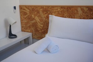 Et hotelværelse med en pænt redt seng, et natbord med en lampe og et panel monteret på væggen.