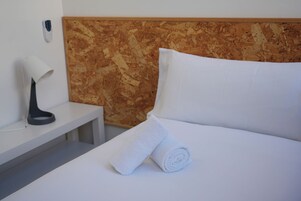 Habitación de hotel con una cama bien tendida, una mesita de noche con lámpara y un panel de control en la pared.