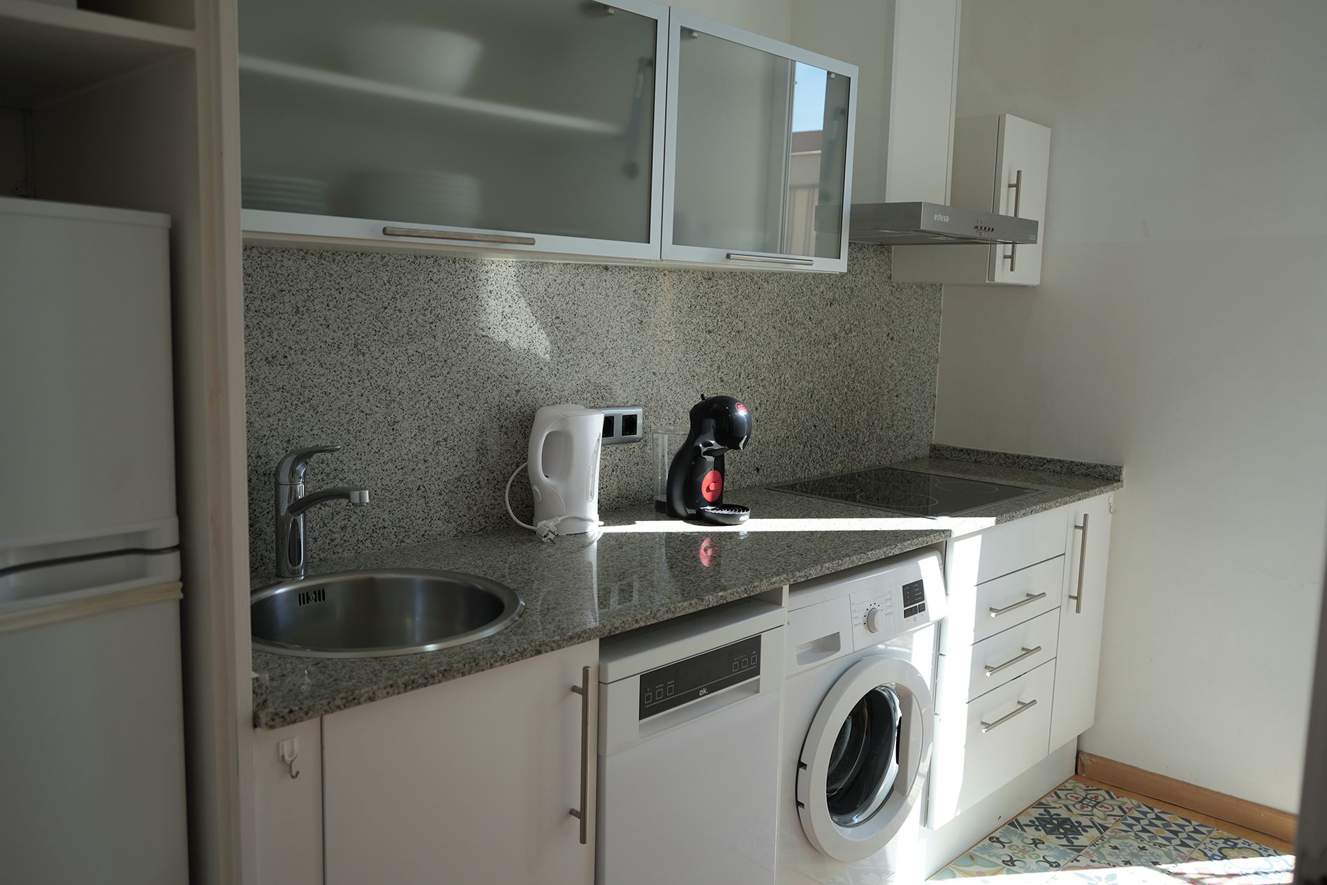 Een kleine keuken met een roestvrijstalen spoelbak, een koffiezetapparaat, een wasmachine en een magnetron.