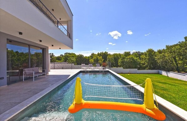 Ein modernes Haus mit Swimmingpool, Sitzgelegenheit im Freien und Blick ins grüne Umland.