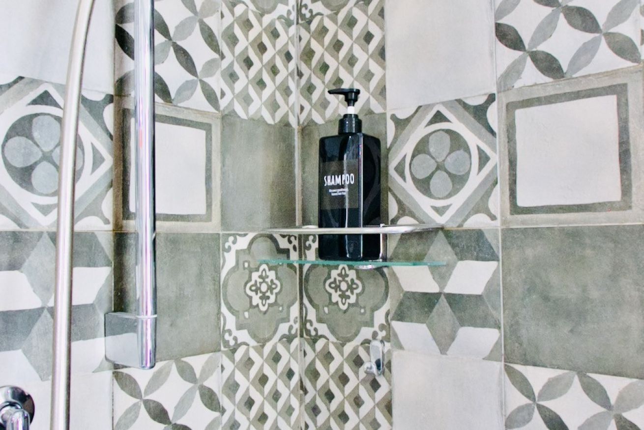 A bathroom with patterned tiles, a glass shelf, and a black shampoo bottle.