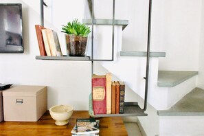 Une bibliothèque avec des livres et une plante en pot, une boîte beige et un bol blanc sur une surface en bois.