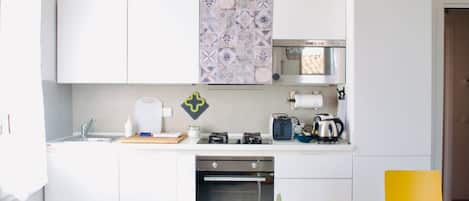 A compact kitchen with white cabinets, a built-in oven, a coffee maker, and a microwave.