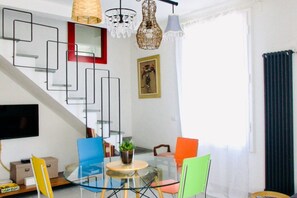 A modern living room with a glass table, colorful chairs, a television, and a staircase with geometric wall art. - Casa Macri, apartment in Santa Maria Novella (Firenze)