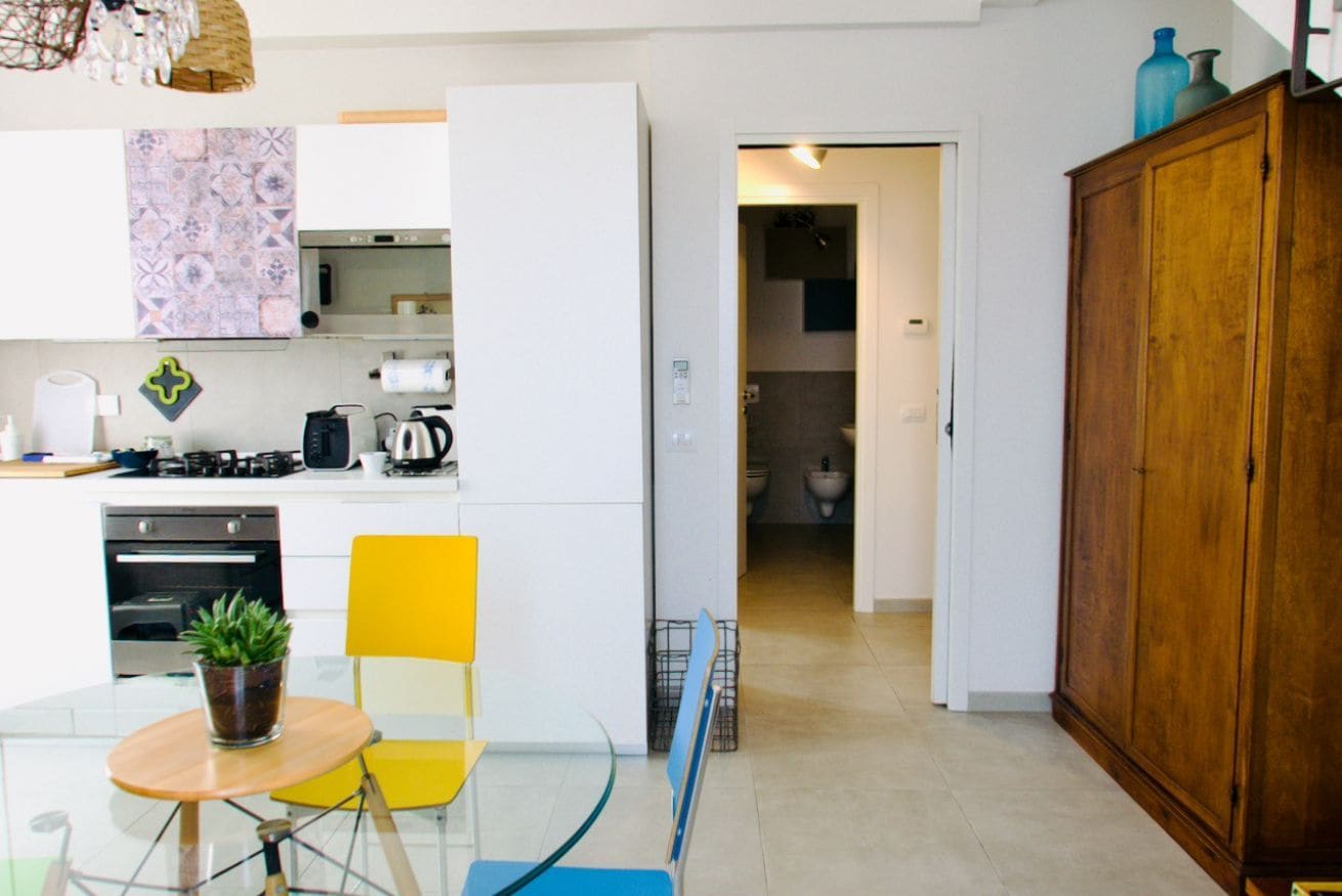 A modern kitchen with white cabinets, a dining table with chairs, and a wooden cabinet.