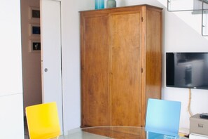 Une pièce avec une armoire en bois, une table en verre et un téléviseur fixé au mur.