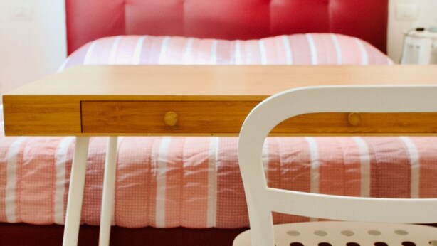 A bed with a red headboard, a wooden bedside table with drawers, and a white chair with a circular backrest. - Casa Macri, apartment in Santa Maria Novella (Firenze)