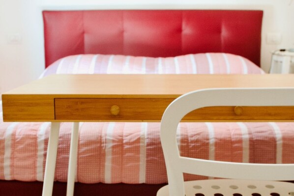 A bed with a red headboard, a wooden bedside table with drawers, and a white chair with a circular backrest. - Casa Macri, apartment in Santa Maria Novella (Firenze)