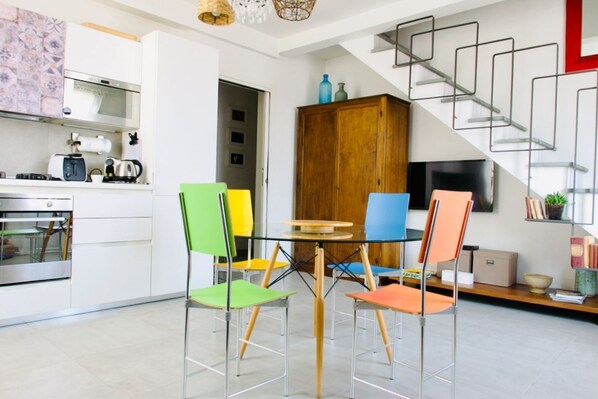 A modern kitchen with white cabinets, a built-in oven, and a dining area with colorful chairs and a glass table. - Casa Macri, apartment in Santa Maria Novella (Firenze)