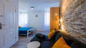 Ein modernes Zimmer mit Backsteinwand, einem Sofa mit gelben Kissen, einem kleinen runden Tisch und einem Bett mit blauer Bettdecke.