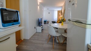 Eine moderne Küche mit integriertem Mikrowellenherd, eine Essecke mit rundem Tisch und Stühlen sowie eine kleine Sitzecke mit Sofa und Fernseher.