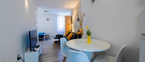 A modern living room with a round dining table, light blue chairs, a sofa with yellow cushions, and a small white table with a yellow vase.