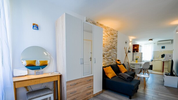Ein modernes Wohnzimmer mit einem Holztisch, einem runden Spiegel, einer Couch mit orangefarbenen Kissen und einer Steinwand.