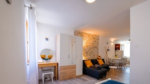 Ein gemütlicher Wohnraum mit Bett, Schreibtisch mit Lampe, Sofa mit Kissen, Kleiderschrank und Essecke mit Stühlen.