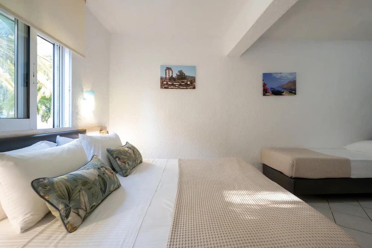 Une chambre d’hôtel moderne avec un grand lit, deux petits lits et une fenêtre donnant sur des palmiers.