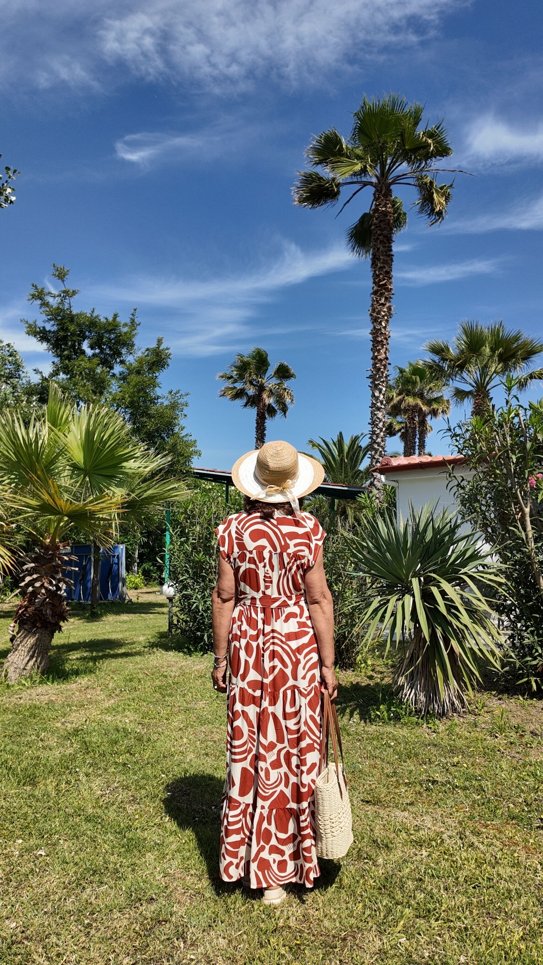 Una persona parada en un jardín con palmeras y cielo despejado.