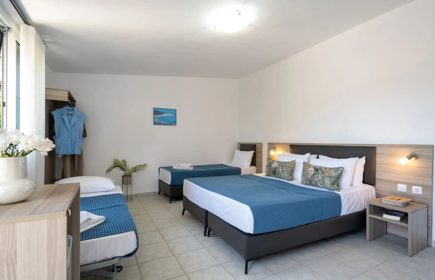 A hotel room with a large bed, two smaller beds, a desk, and a wardrobe.
