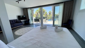 A modern hotel room with a large bed, a sofa, a TV, and a balcony with a pool view. - PALMA VILLAGE HOTEL by Greek Pride (Kassandra)