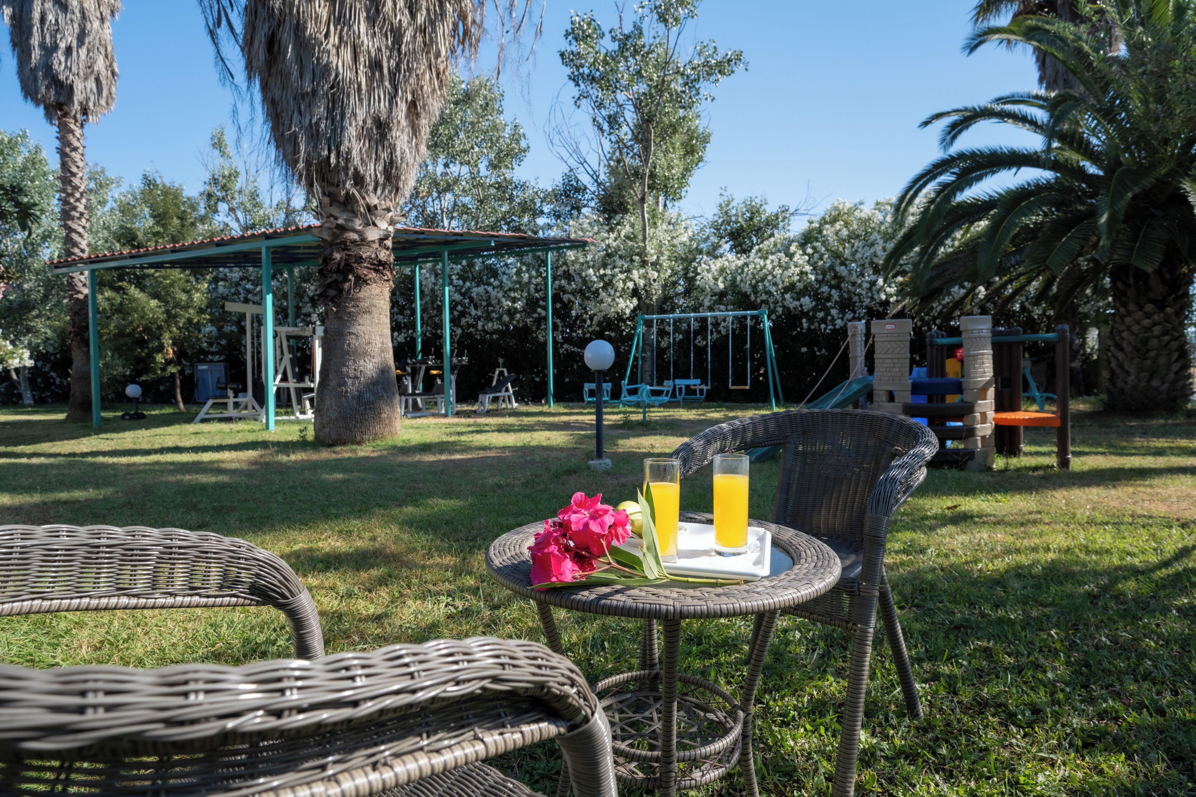 A wicker chair with a tray of drinks and a flower, a swing set, and a covered play area in a park.