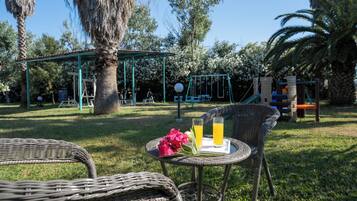 A wicker chair with a tray of drinks and a flower, a swing set, and a covered play area in a park.