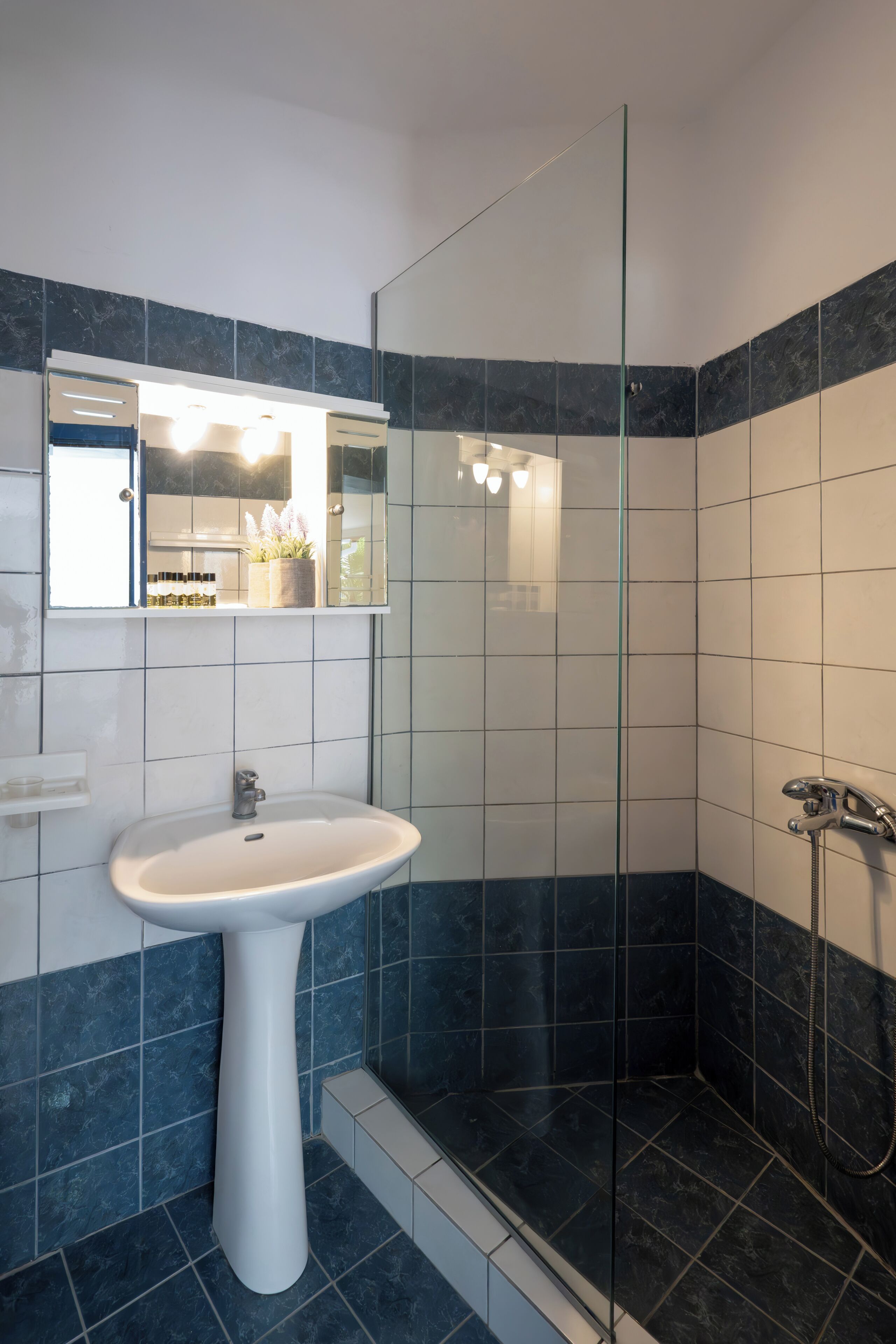 Un baño con lavamanos blanco, cabina de ducha de vidrio y un espejo sobre el lavamanos.