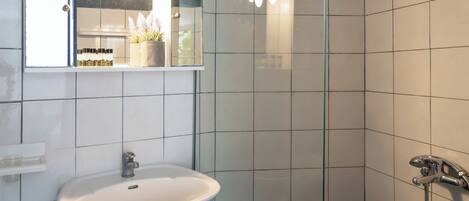 Un baño con lavamanos blanco, cabina de ducha de vidrio y un espejo sobre el lavamanos.