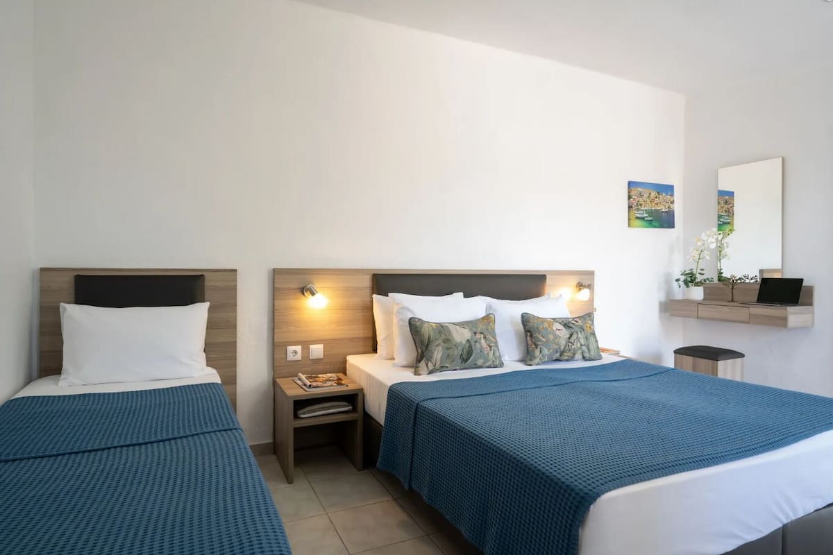 Une chambre d’hôtel avec deux lits, chacun dot é d’une tête de lit en bois, d’une table de chevet et d’une étagère murale sur laquelle se trouvent un ordinateur portable et une plante.