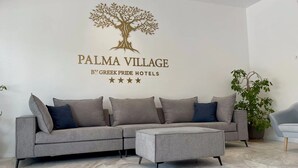 A reception area with a grey sofa, a small table, and a potted plant. - PALMA VILLAGE HOTEL by Greek Pride (Kassandra)