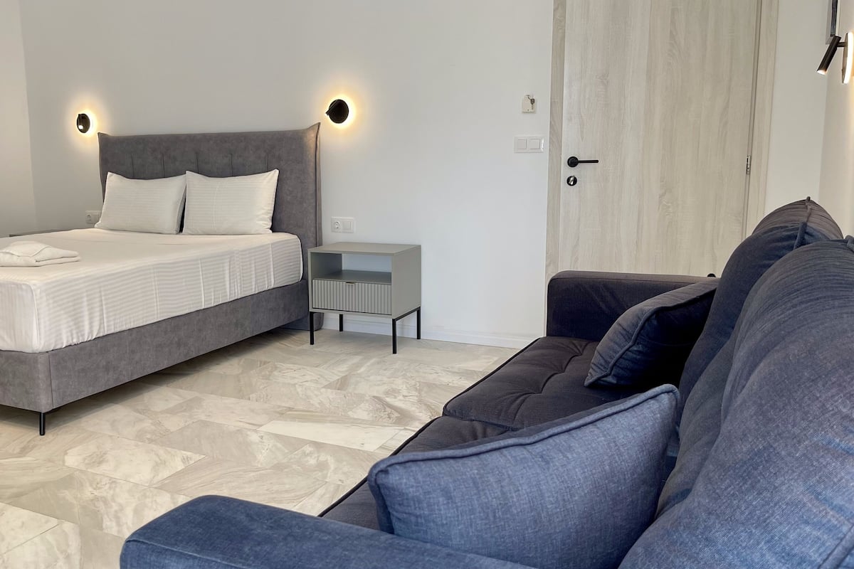 Une chambre à coucher moderne avec un lit, une table de chevet, un canapé et une porte.