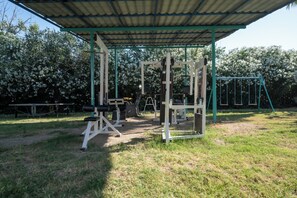 An outdoor gym with exercise equipment, a covered area, and a swing set. - PALMA VILLAGE HOTEL by Greek Pride (Kassandra)