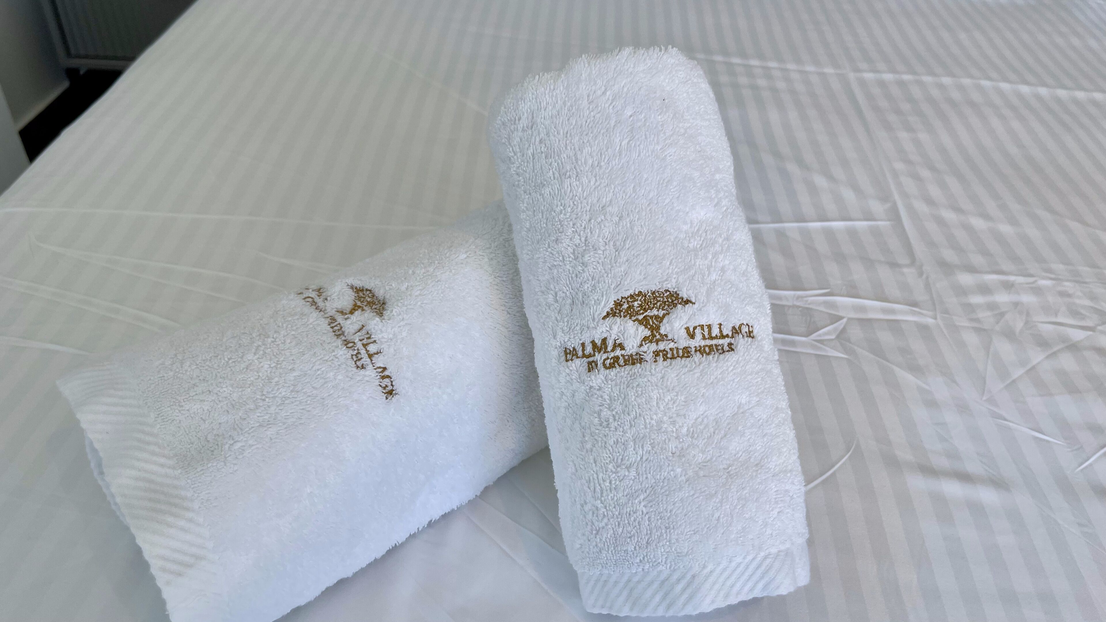Two rolled white towels with embroidered text on a bed.