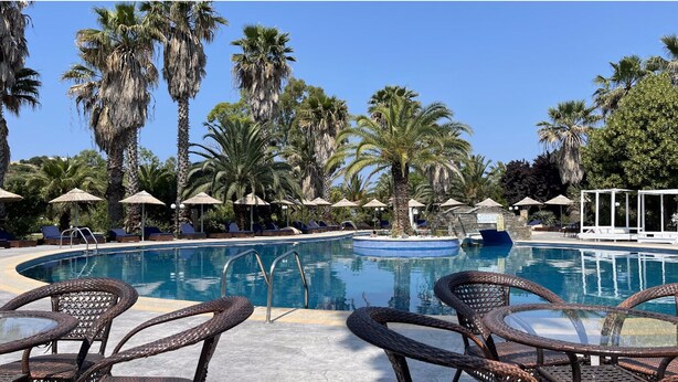 A poolside area with lounge chairs and umbrellas, surrounded by palm trees. - PALMA VILLAGE HOTEL by Greek Pride (Kassandra)