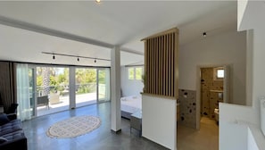 A spacious living area with a large sliding glass door leading to a balcony, a bed with white linens, and a modern kitchen area. - PALMA VILLAGE HOTEL by Greek Pride (Kassandra)