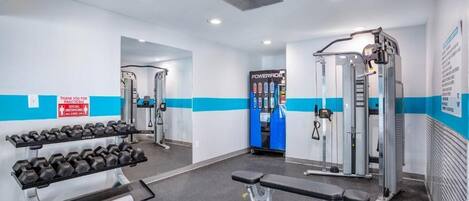 Une salle de sport équipée de matériel de musculation, de bancs et d’un réfrigérateur rempli de boissons Powerade.