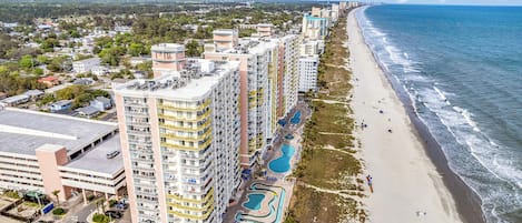 A beachfront hotel with multiple high-rise buildings, a swimming pool area, and a sandy beach.