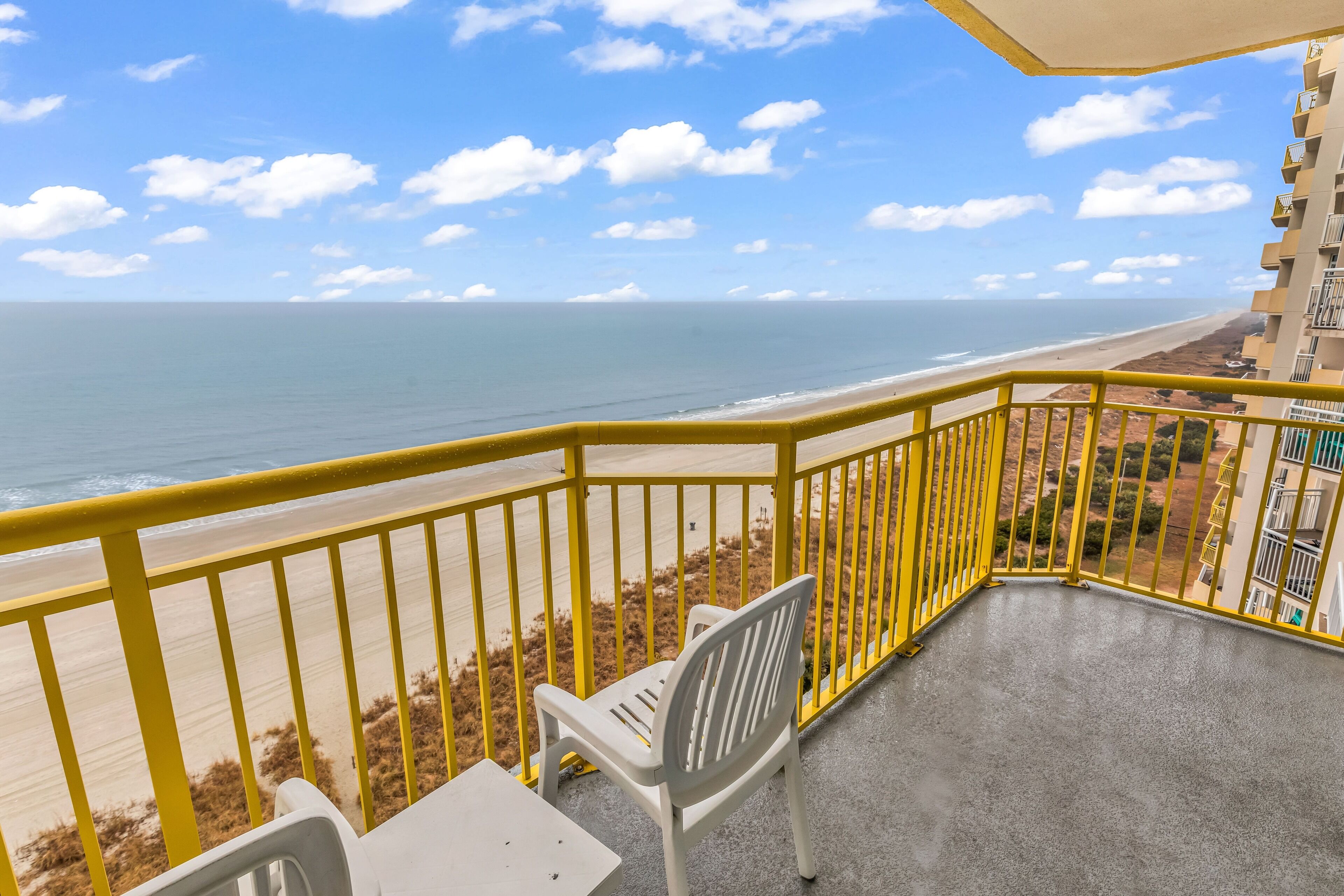 Un balcon avec une rambarde jaune donnant sur une plage.
