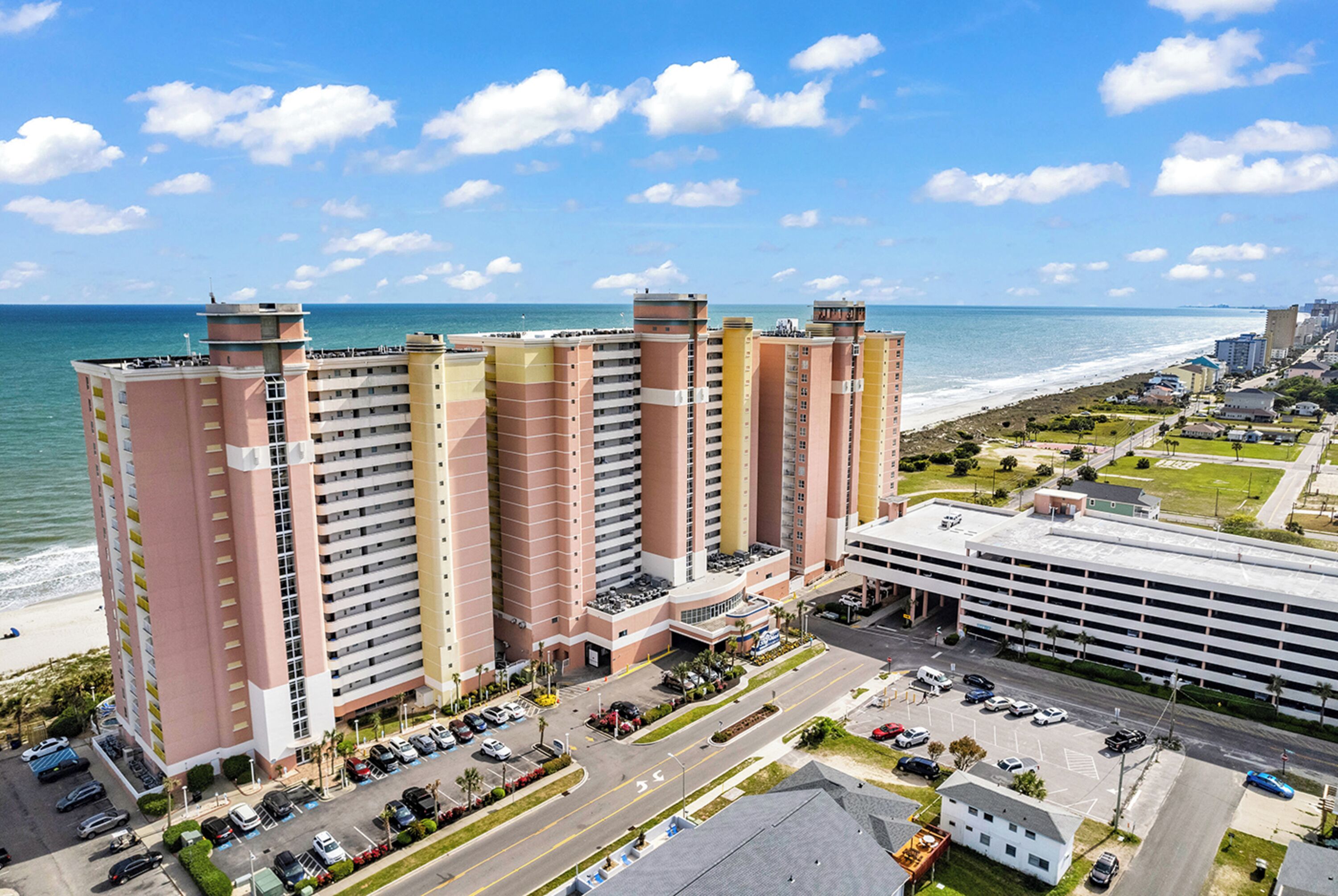 A high-rise hotel with multiple floors, a parking lot, and a view of the beach.